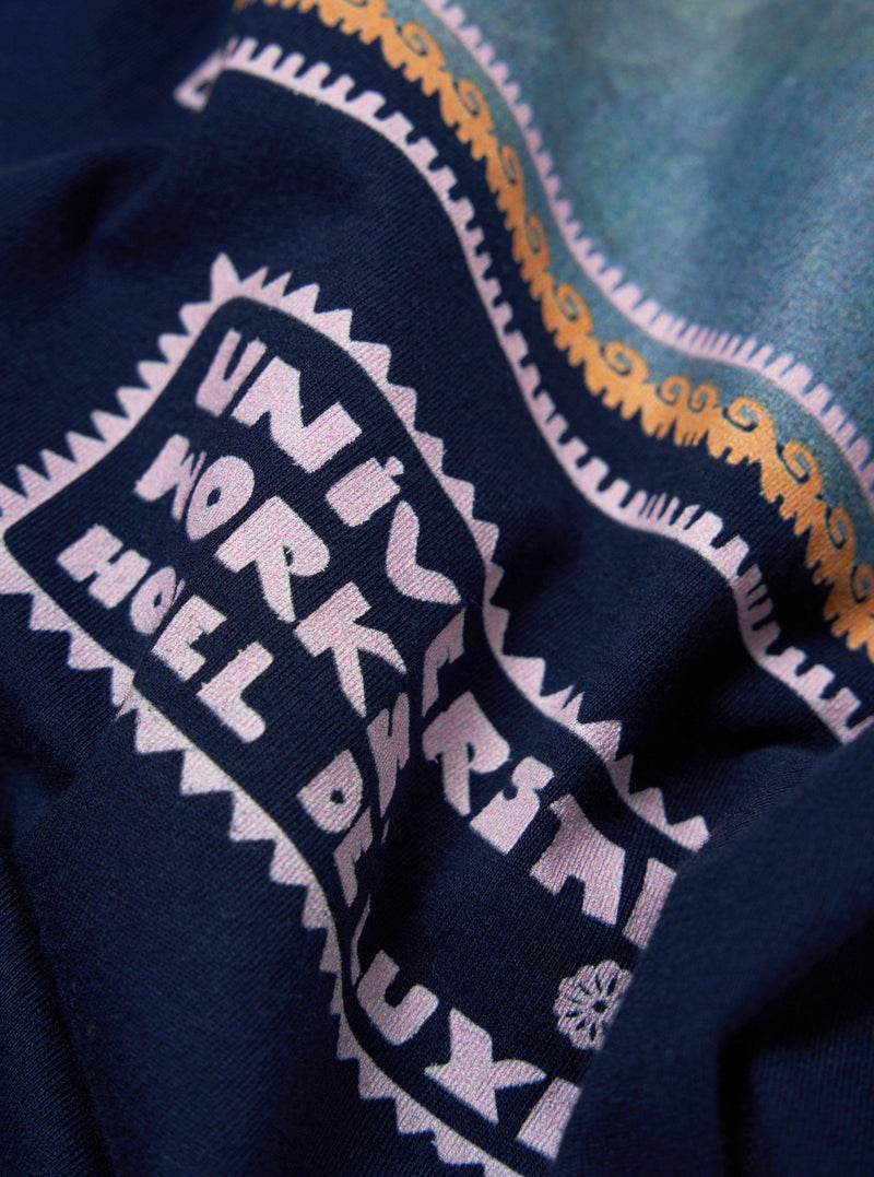 Close-up of the Navy/Pink Single Jersey Pickup Print Tee fabric. The navy jersey features a pink print. The background is a soft, blurred gradient.
