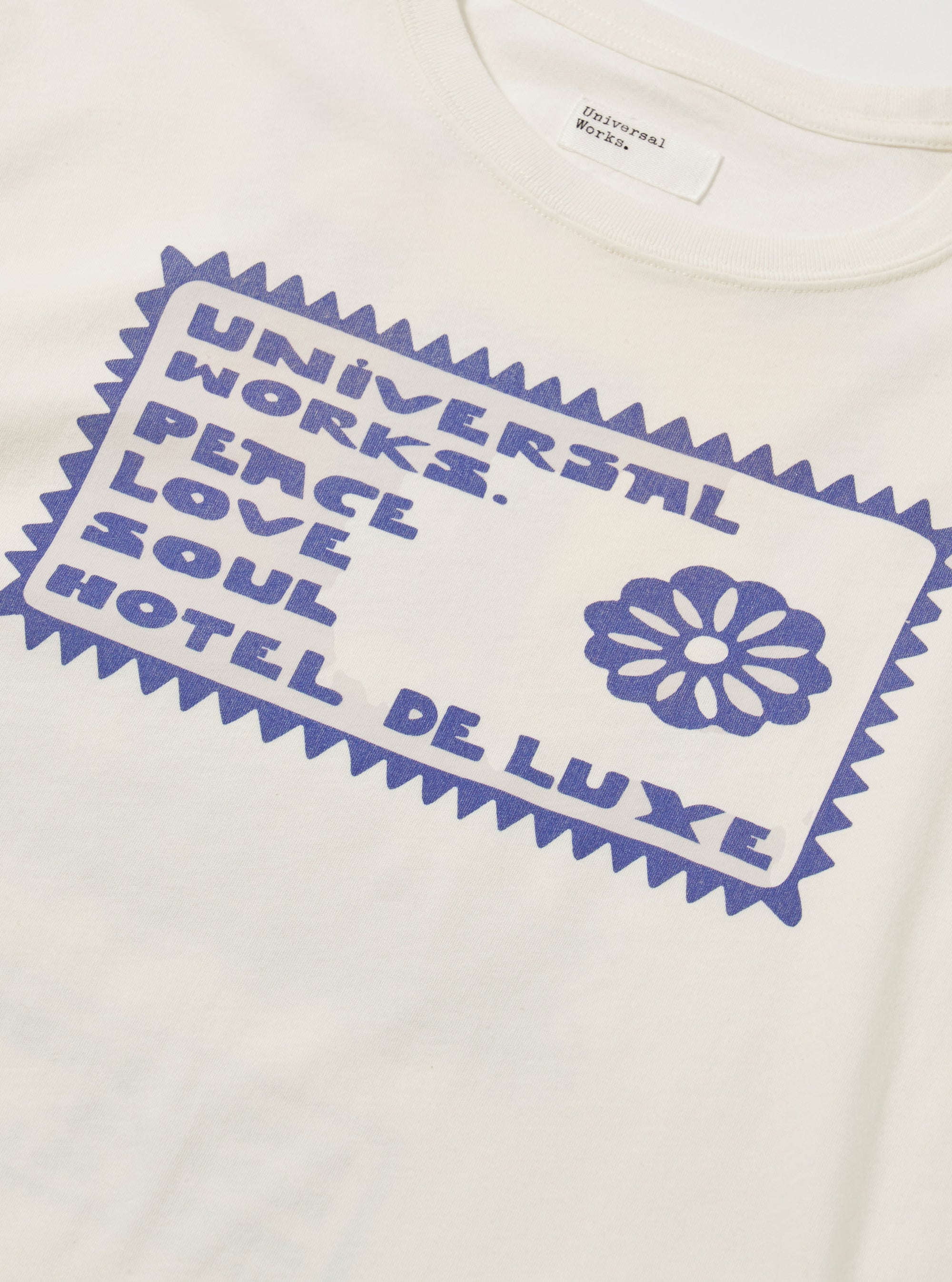 Close-up of the Ecru/Yellow Single Jersey Pickup Print Tee. The tee is ecru with a blue graphic print. The background is a plain white surface.
