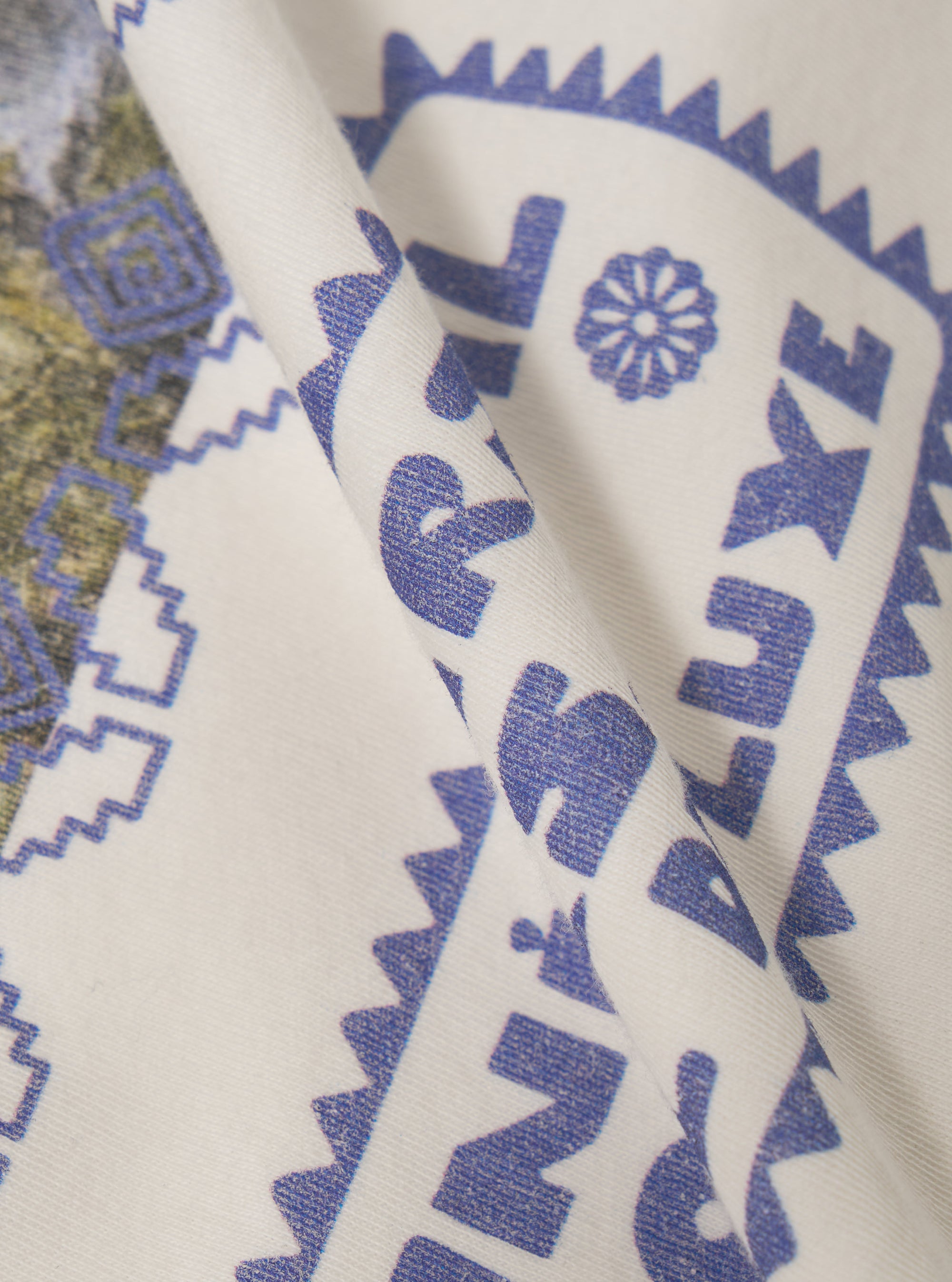 Close-up of the Ecru/Yellow Single Jersey Pickup Print Tee fabric. The ecru tee features a blue print. The fabric is folded, showcasing the soft single jersey material.