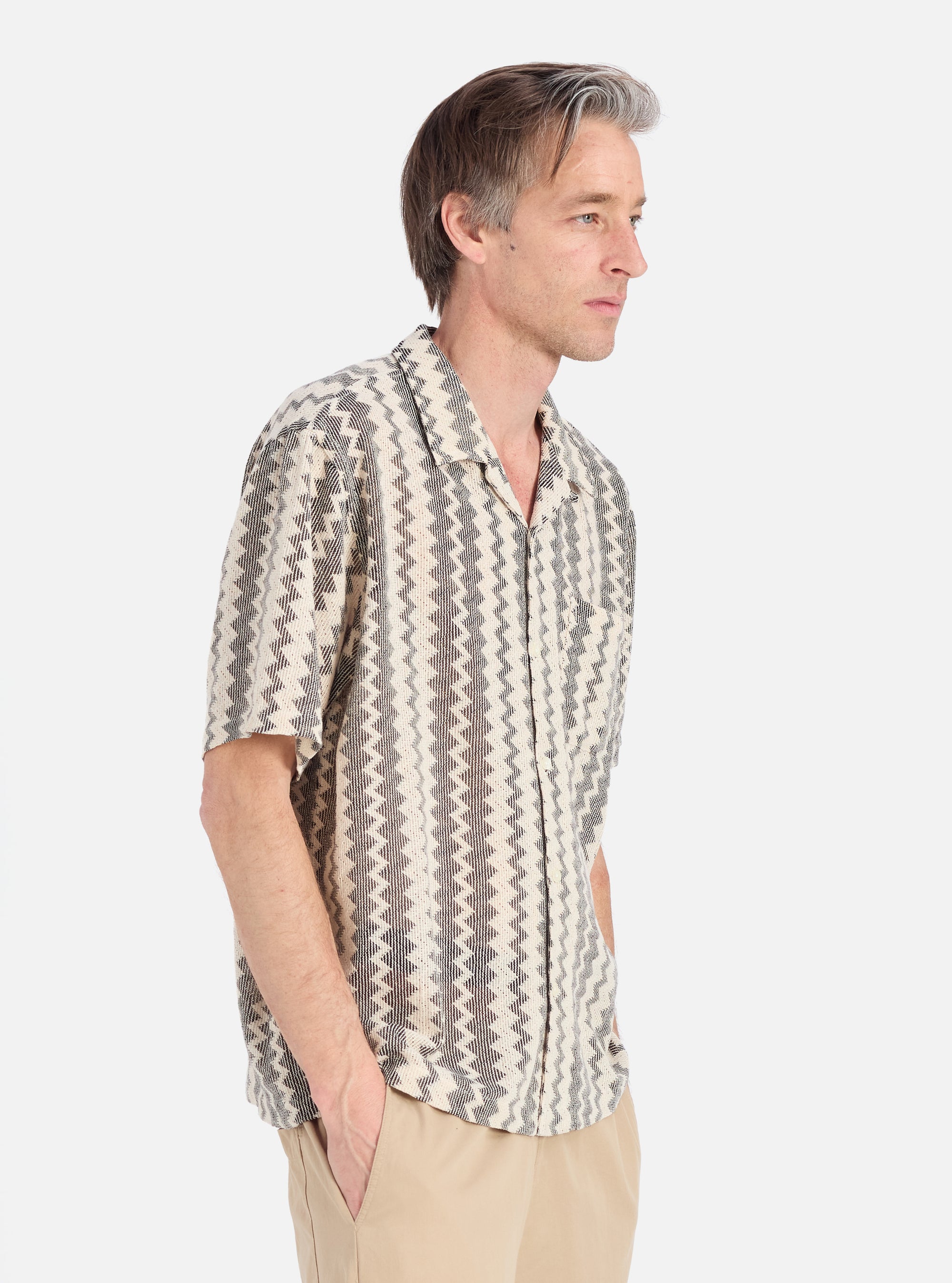 A man in profile on a white background wears the Charcoal Cotton Lattice Road Shirt. The shirt has a black and white geometric pattern. He wears khaki pants.