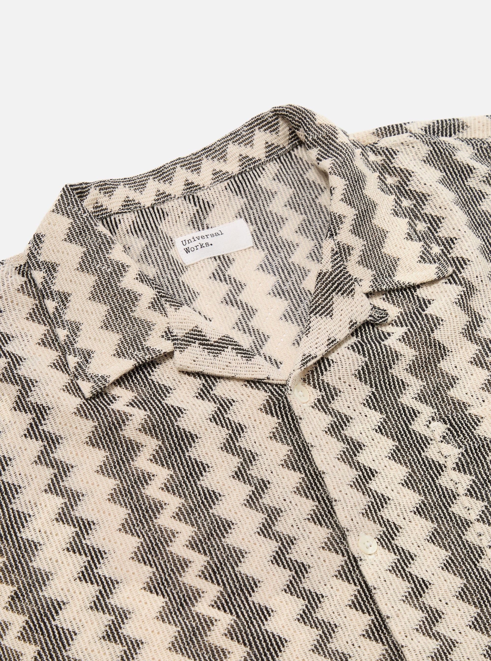 Close-up of the Charcoal Cotton Lattice Road Shirt. The shirt has a black and cream lattice pattern. Cotton material. The shirt is laid on a white surface.
