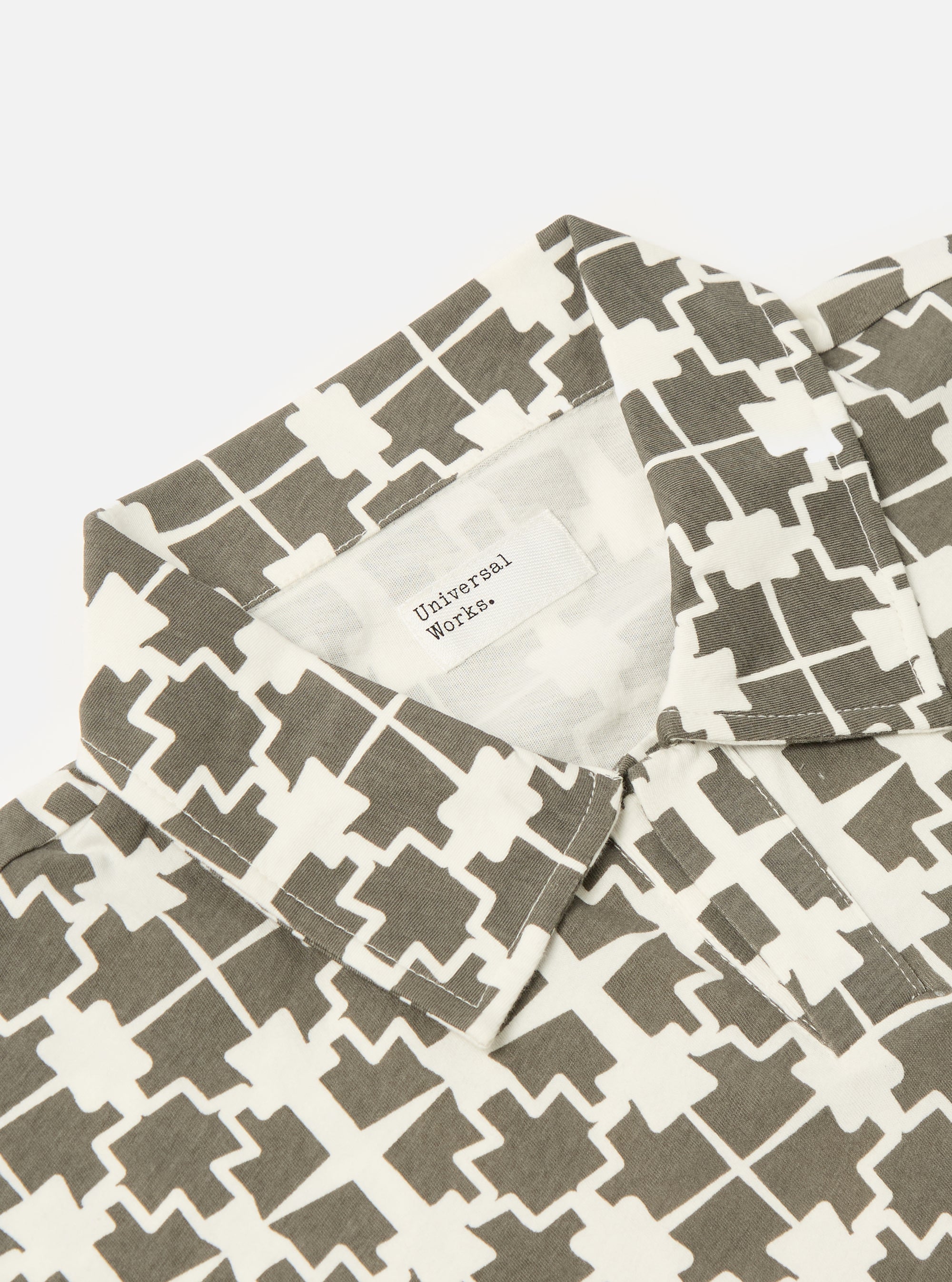 Close-up of the Ecru/Mud Mitla Print Jersey Newlyn Polo on a white background. The polo features a geometric print in ecru and mud. The collar and tag are visible.