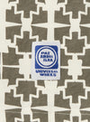 Close-up of the Ecru/Mud Mitla Print Jersey Newlyn Polo, showcasing the geometric pattern and fabric texture. A Universal Works label is visible. 