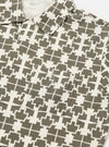 Close-up of the Ecru/Mud Mitla Print Jersey Newlyn Polo. The polo shirt features a unique geometric pattern in ecru and mud tones. Made from soft jersey material, it has a relaxed fit and a chest pocket.
