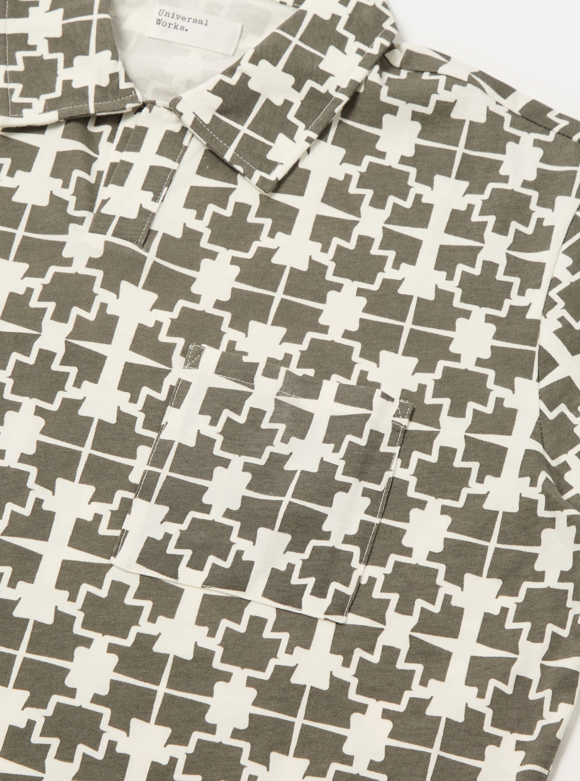 Close-up of the Ecru/Mud Mitla Print Jersey Newlyn Polo. The polo shirt features a unique geometric pattern in ecru and mud tones. Made from soft jersey material, it has a relaxed fit and a chest pocket.
