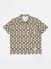 The Ecru/Mud Mitla Print Jersey Newlyn Polo shirt, featuring a geometric pattern, is laid flat on a white background. The polo is ecru with a mud-colored print.