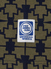 Close-up of the Navy/Mud Mitla Print Jersey Newlyn Polo fabric, showcasing the intricate pattern and the 'Universal Works' label. The jersey material is soft and textured.