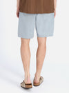 Back view of a model wearing the Indigo Reworked Jean Cloth Alva Short, light blue denim, paired with brown sandals. Shot on a white background.