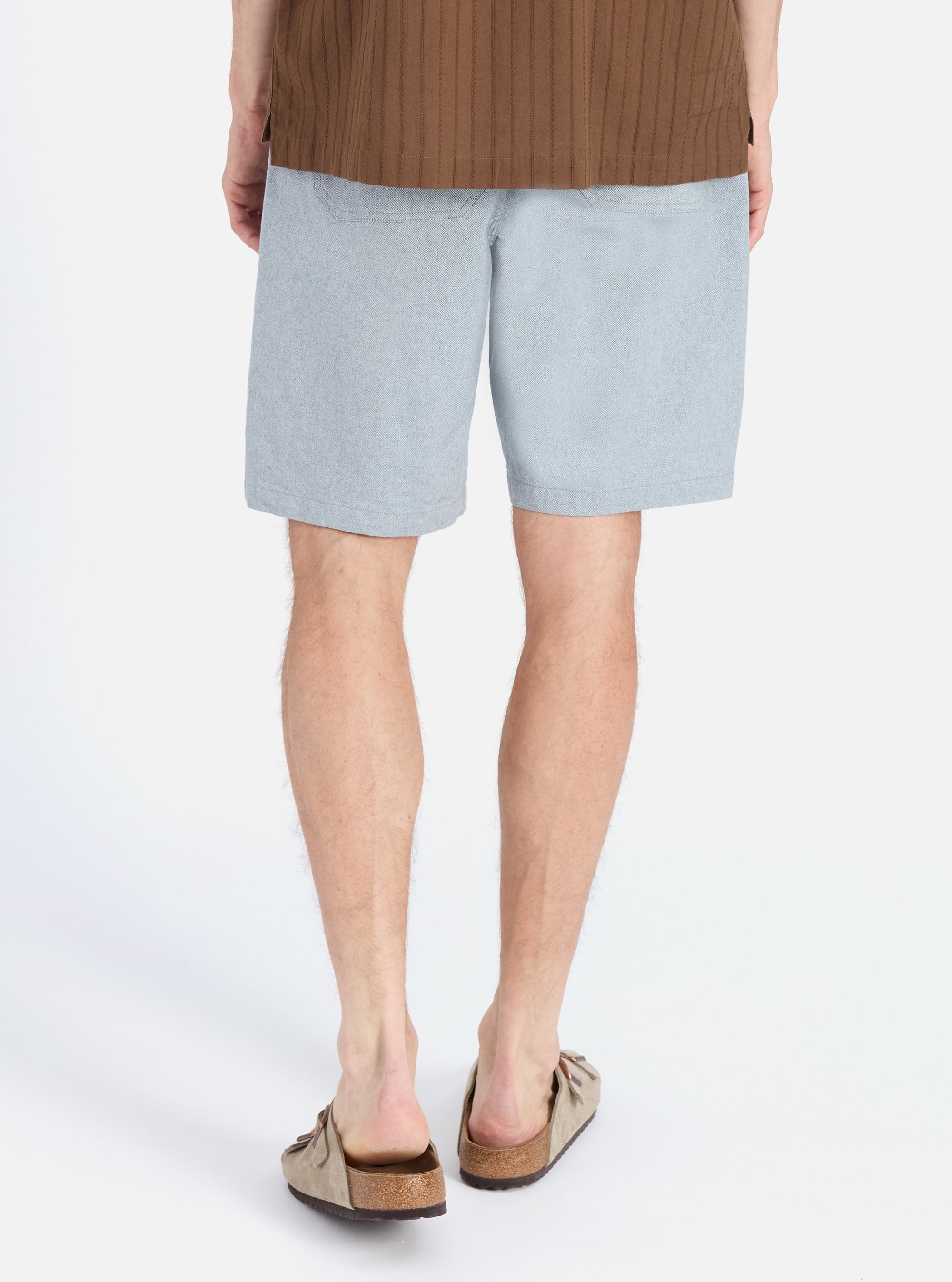 Back view of a model wearing the Indigo Reworked Jean Cloth Alva Short, light blue denim, paired with brown sandals. Shot on a white background.