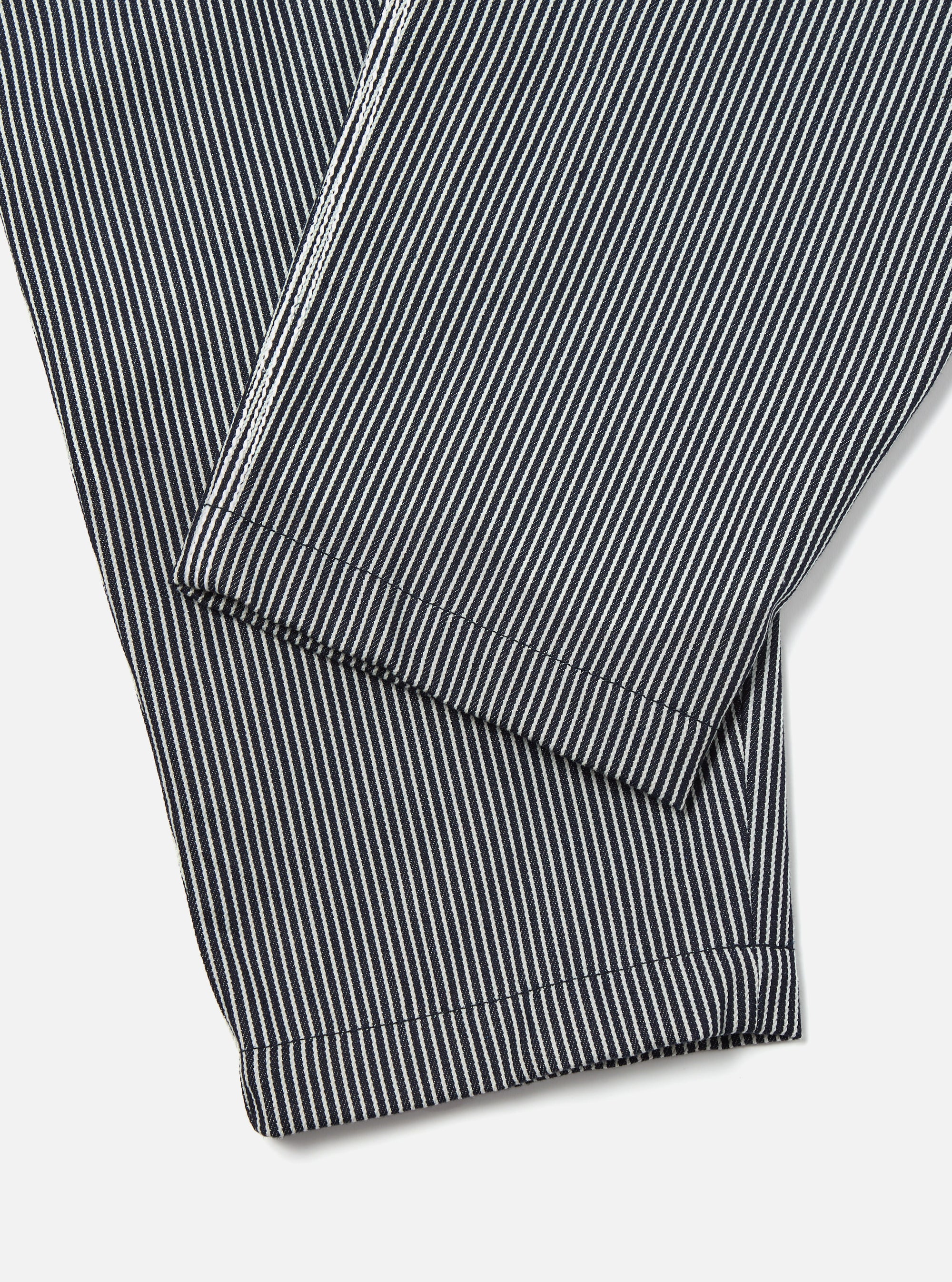Close-up of the Indigo Hickory Stripe Denim Pleated Track Pant on a white surface, showcasing the fabric's texture and pleated design.