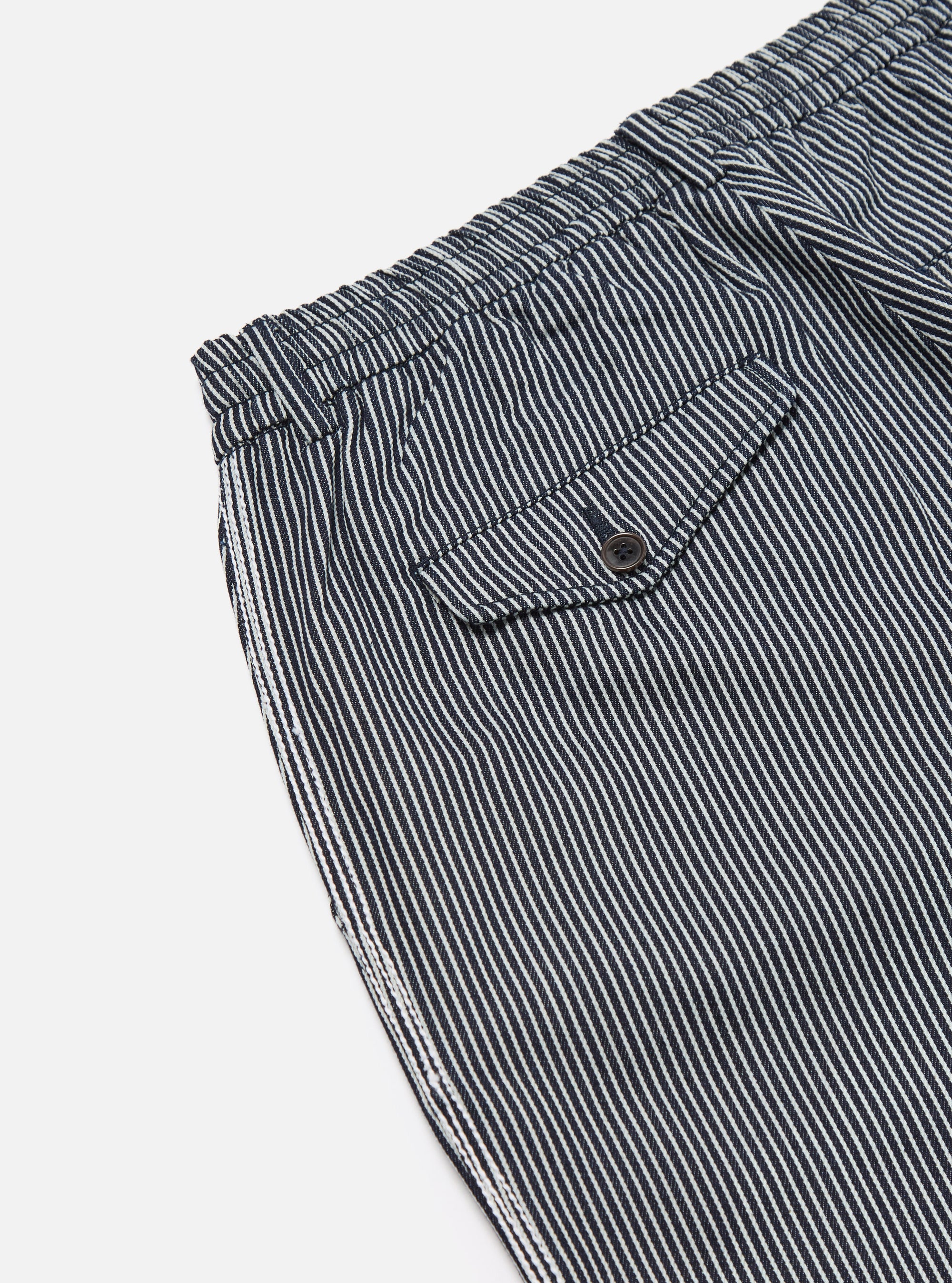 Close-up of Indigo Hickory Stripe Denim Pleated Track Pant on white. Features include striped denim, pleated design, and a small pocket. 