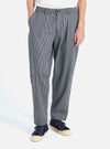 A man stands in front of a white background modeling the Indigo Hickory Stripe Denim Pleated Track Pant. The striped pants are paired with blue sneakers.