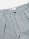 Close-up of the Indigo Reworked Jean Cloth Oxford Pant in light blue. Features an elastic waistband, button closure, and pleated design. Shot on a white background.