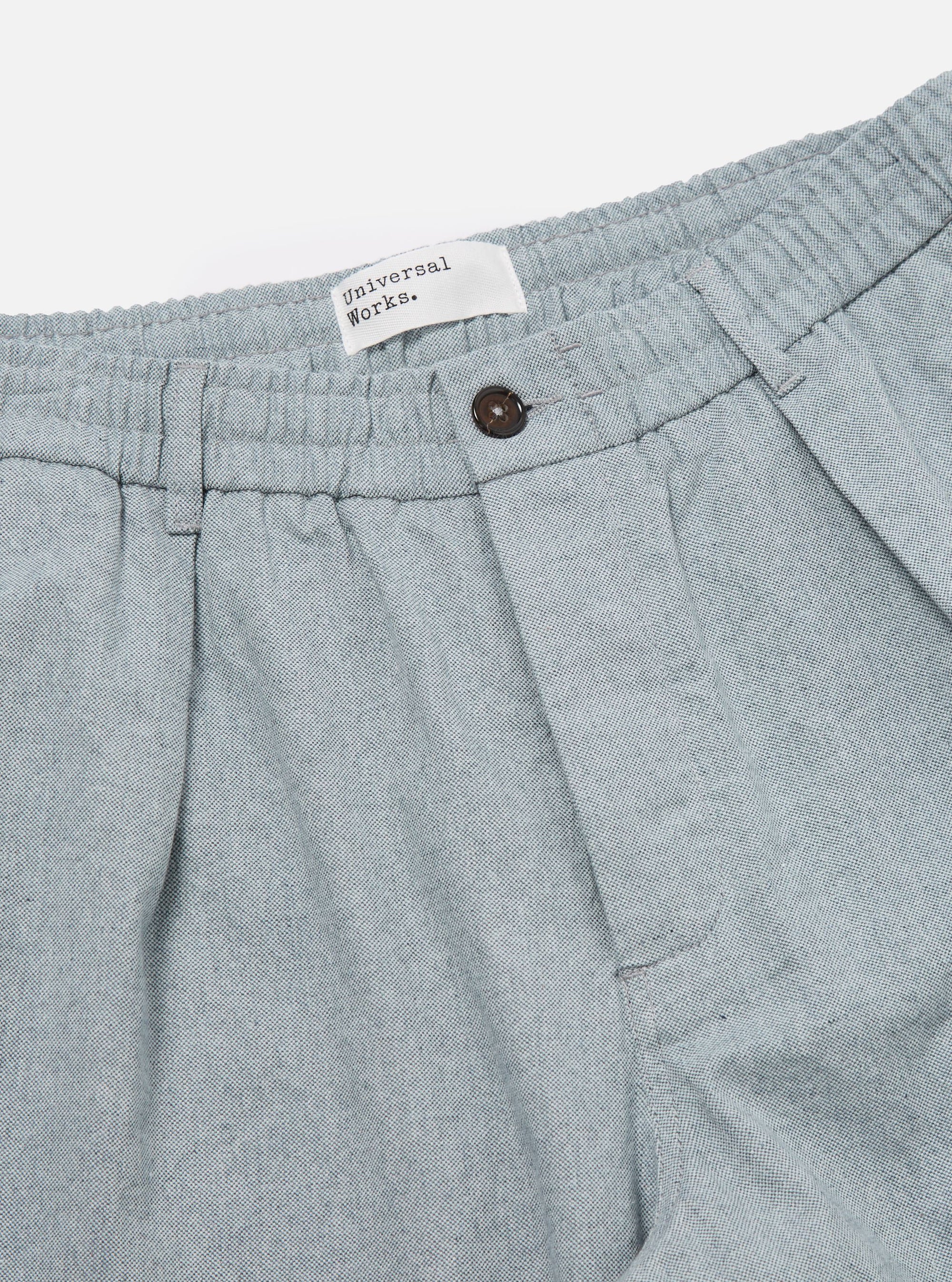 Close-up of the Indigo Reworked Jean Cloth Oxford Pant in light blue. Features an elastic waistband, button closure, and pleated design. Shot on a white background.