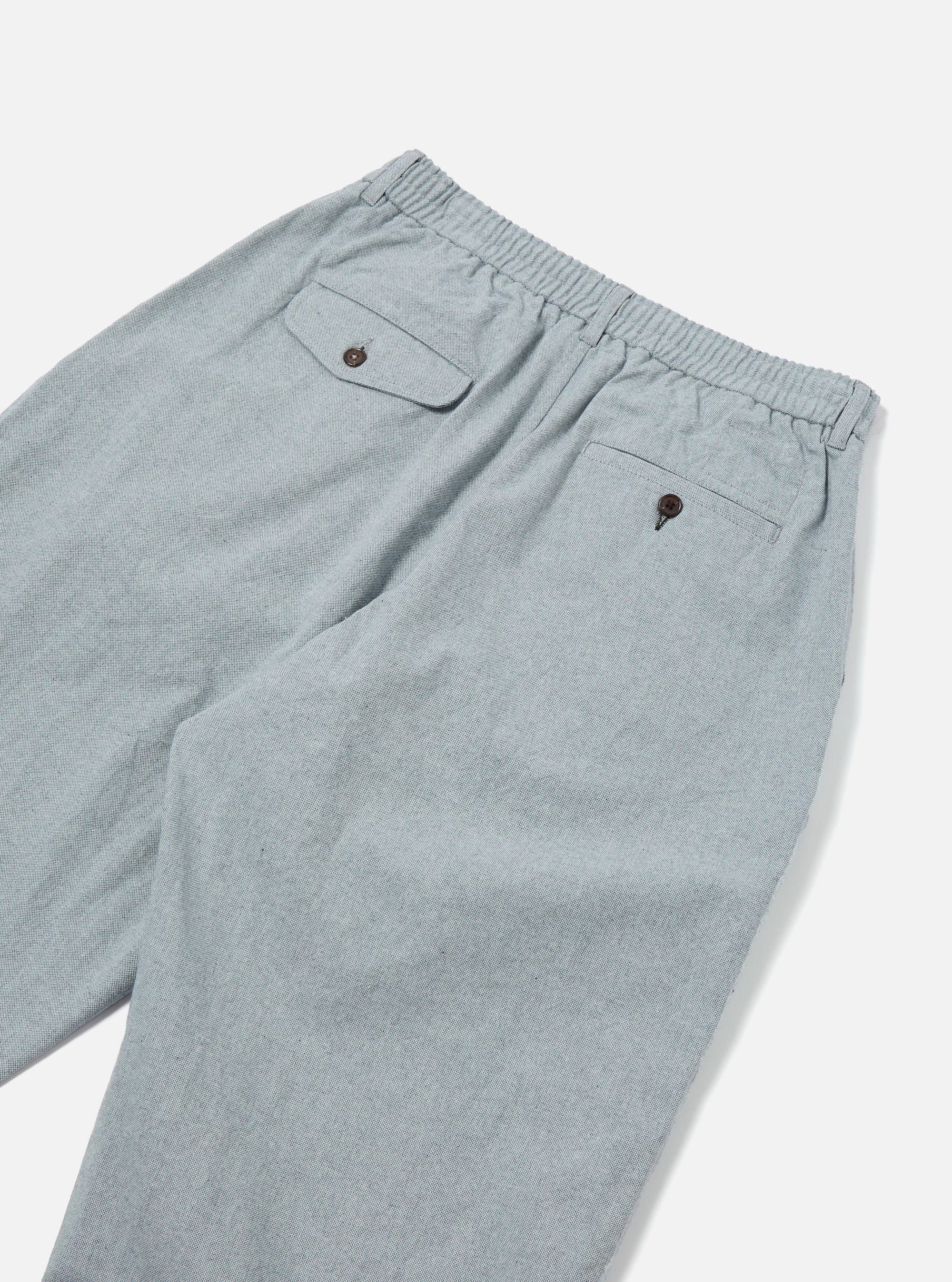 Close-up of the back of Indigo Reworked Jean Cloth Oxford Pant in light blue. Features an elastic waistband and buttoned pockets, laid on a white surface.