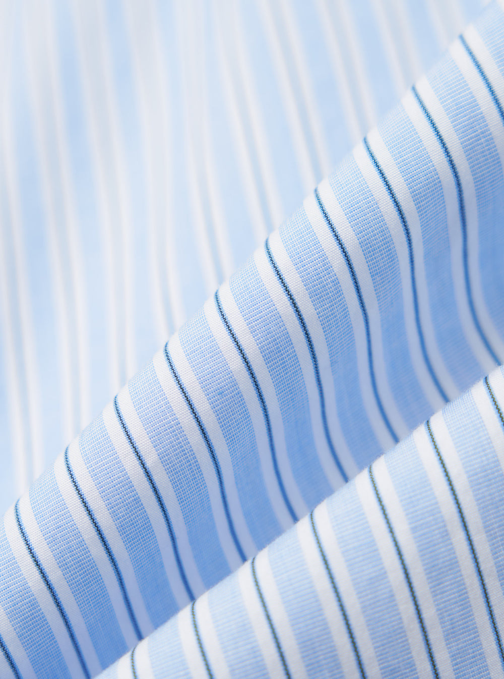 Close-up of the Blue Office Stripe Patched Lazy Day Shirt fabric. Light blue and white stripes with a subtle texture. The shirt is neatly folded, showcasing the pattern.