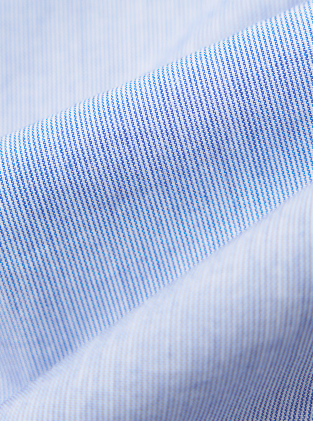 Close-up of the Blue Classic Stripe Lazy Day Shirt fabric. Light blue and white stripes create a soft, textured look. The material is neatly folded on a plain surface.