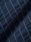 A close-up fabric swatch of the Navy Chester Stripe Two Button Jacket displays a detailed view of the navy blue cotton material with fine, vertical white stripes. The image highlights the texture and weave of the fabric.