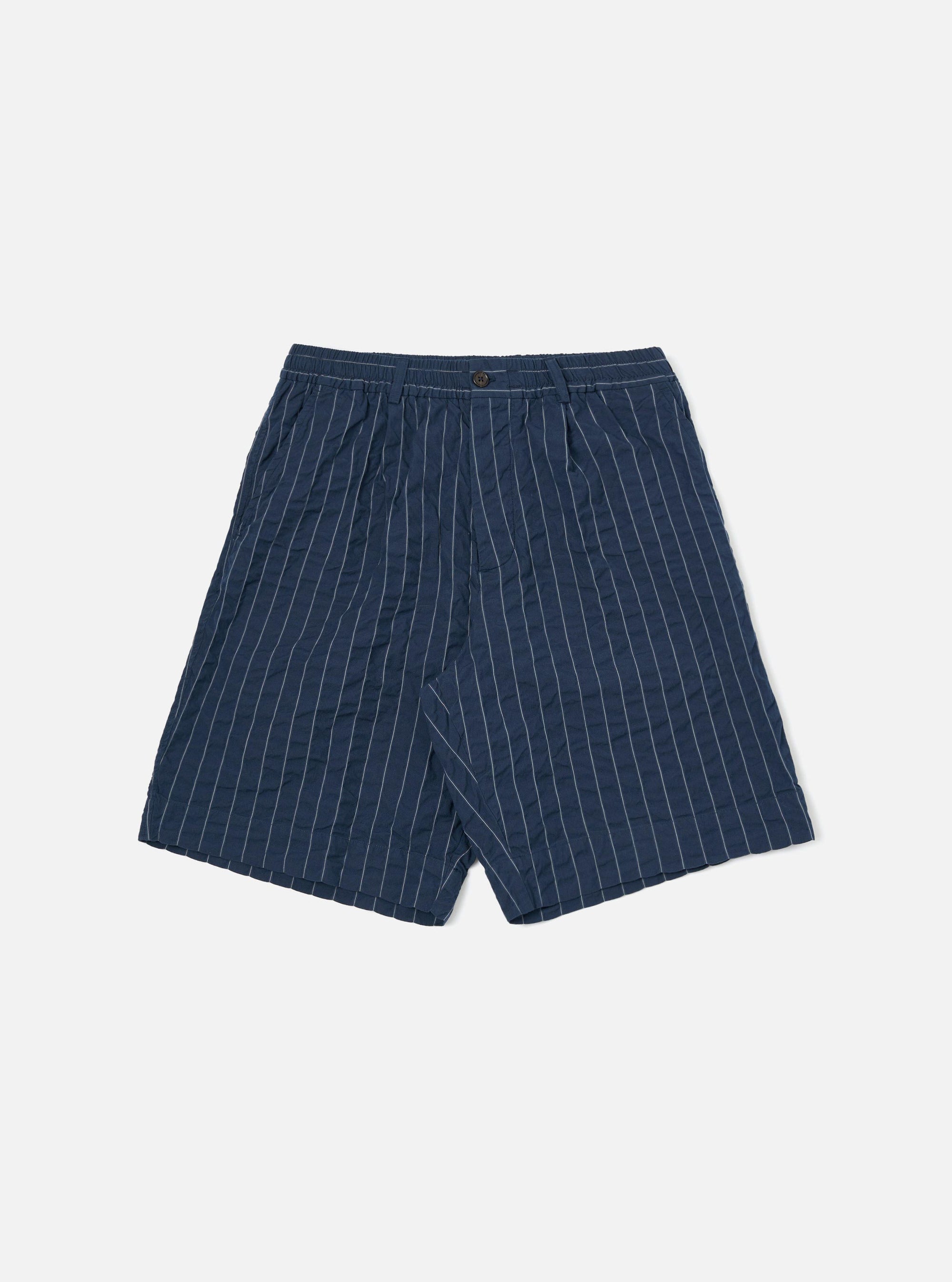 A pair of Navy Chester Stripe Pleated Track Shorts is shown laid flat against a solid white background. The shorts feature a vertical white pinstripe pattern on a navy base, an elasticated waistband with a button closure, a single pleat on each leg, and two side pockets.