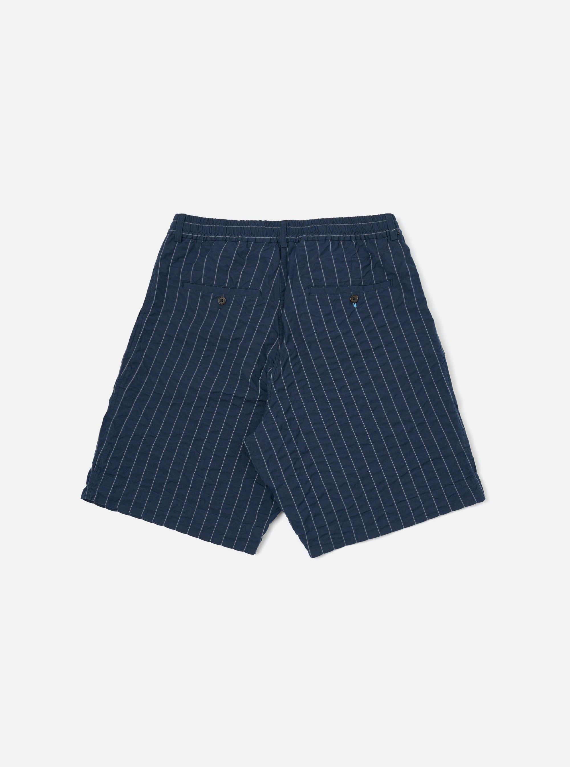 A pair of Navy Chester Stripe Pleated Track Shorts is shown from the back, laid flat against a plain white background. The shorts feature a subtle vertical stripe pattern, an elasticated waistband with a central hang loop, and two rear patch pockets.