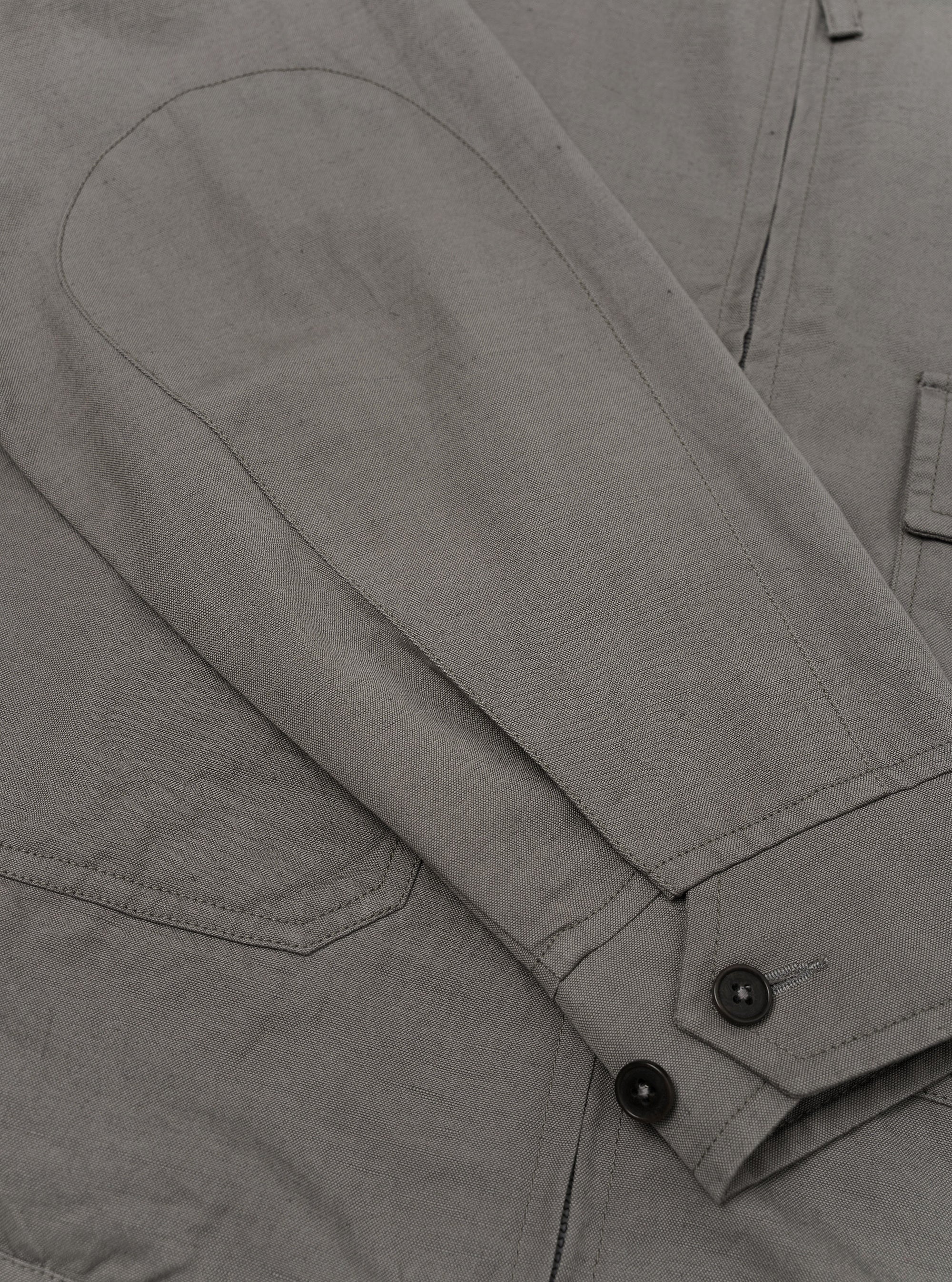 A Mid Grey Linen Slub Weave E130 Jacket is shown from the back, laid flat against a solid white background. The image highlights the straight hem, the simple construction of the back panel, and the textured appearance of the linen-cotton slub fabric.