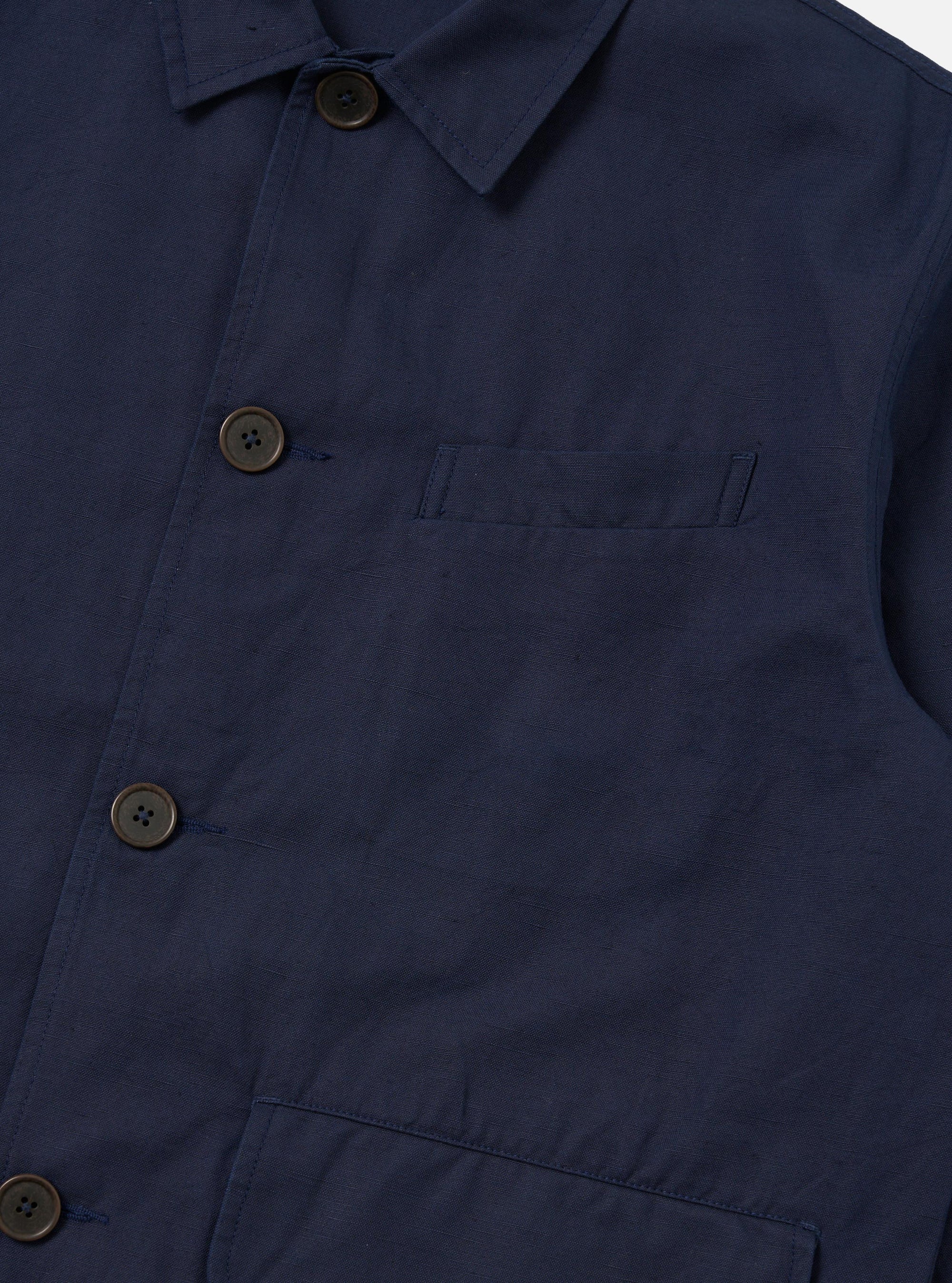 A close-up detail shot of the Navy Linen Slub Weave Franck Jacket against a plain white background. The image focuses on the textured navy blue linen-cotton blend fabric, highlighting the irregular slubbed weave and the clean stitching of a patch pocket and the garment's edge.