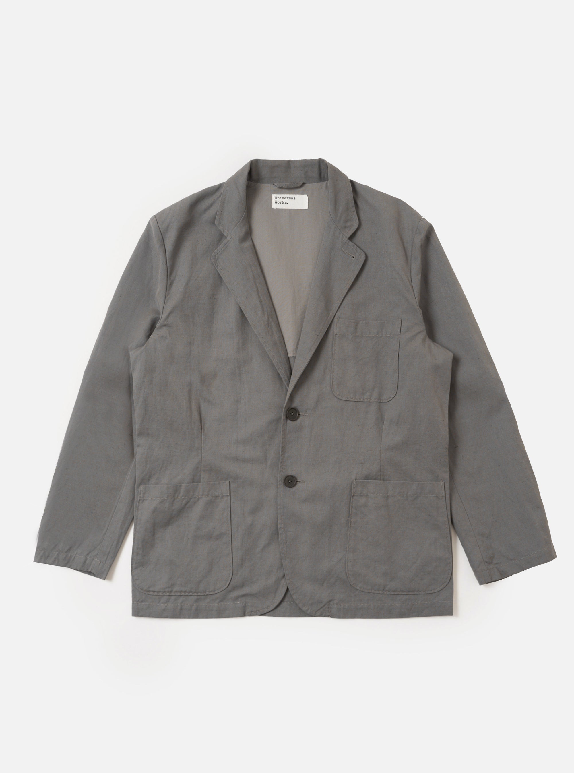 The Mid Grey Linen Slub Weave Two Button Jacket is shown as a flat lay against a solid white background. The jacket features a notch lapel, a two-button front closure, and two large patch pockets at the waist. The mid-grey fabric has a visible, textured slub weave throughout.