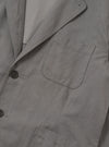 The Mid Grey Linen Slub Weave Two Button Jacket is displayed as a flat lay against a solid white background. The jacket features a two-button front closure, a notched lapel, and two large patch pockets at the hips. The mid-grey fabric has a visible, textured slub weave.