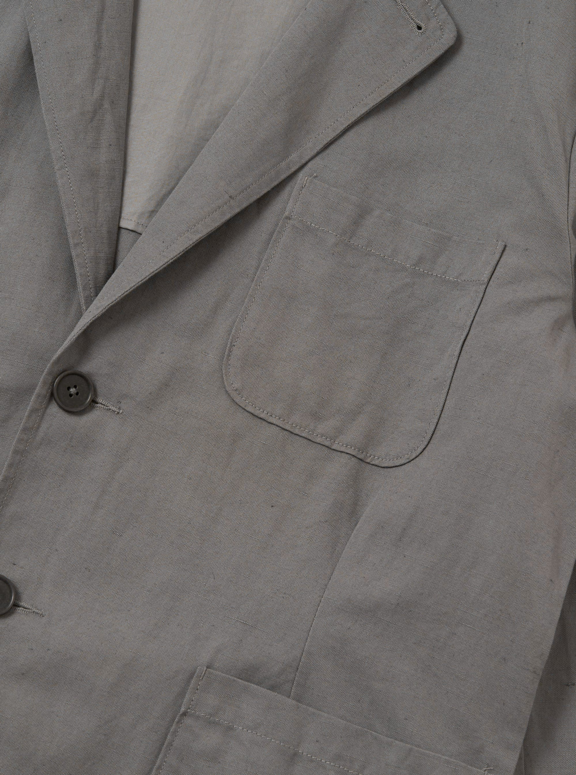 The Mid Grey Linen Slub Weave Two Button Jacket is displayed as a flat lay against a solid white background. The jacket features a two-button front closure, a notched lapel, and two large patch pockets at the hips. The mid-grey fabric has a visible, textured slub weave.