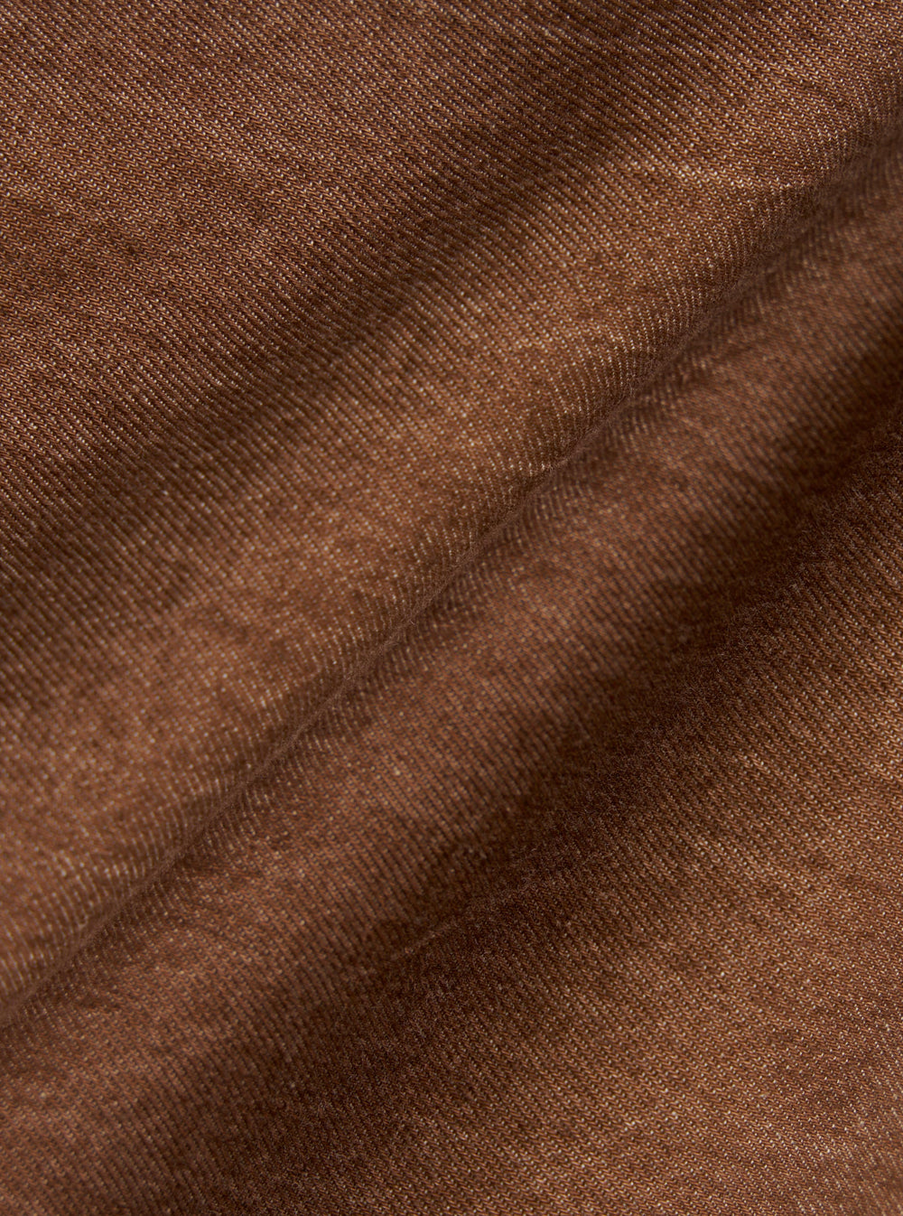 A close-up fabric swatch of the brown Meco denim used for the OG Bakers Jacket shows a detailed view of the material's texture and earthy brown color. The image focuses entirely on the weave of the recycled cotton fabric.