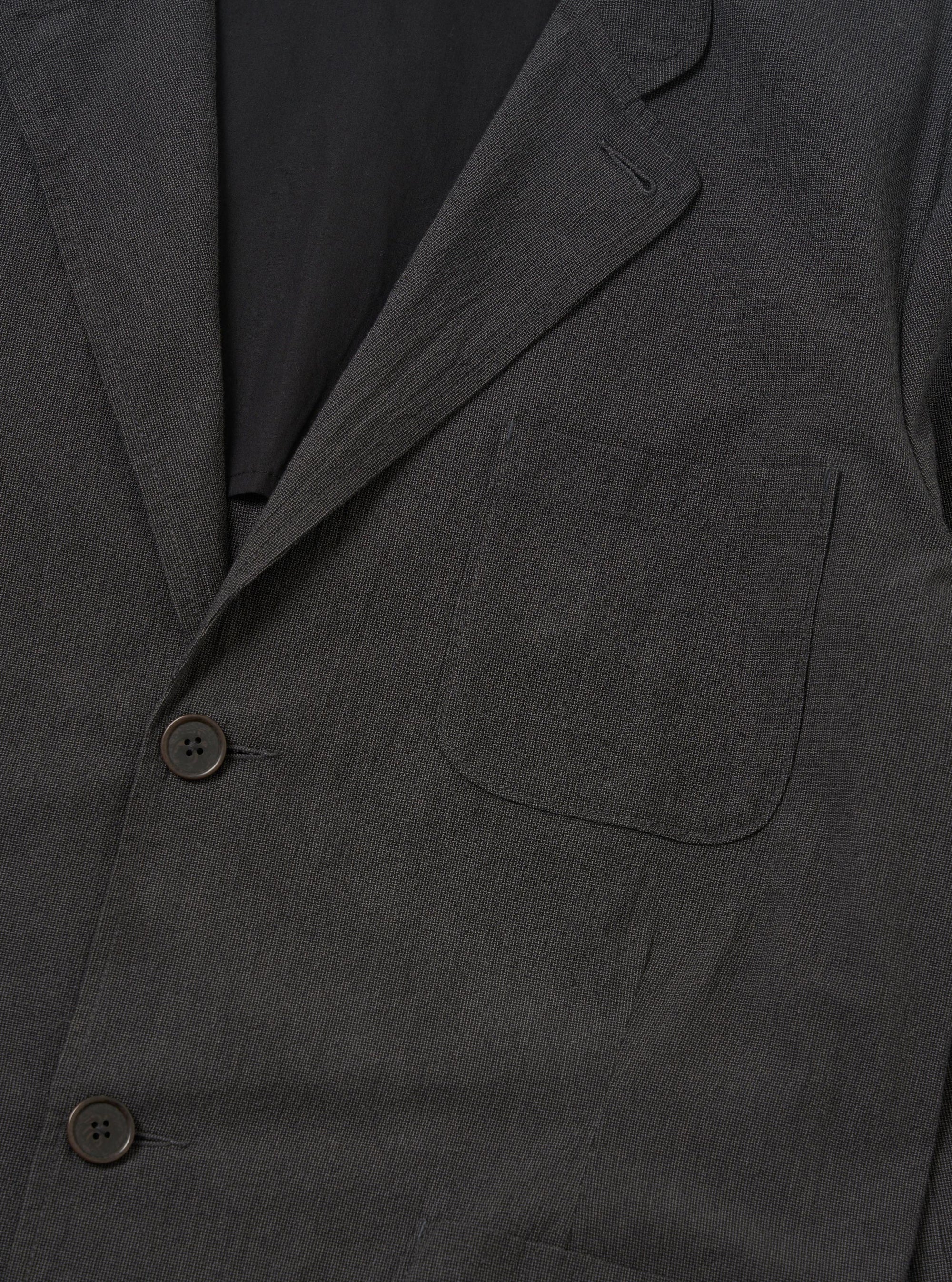 A back view of the Charcoal Seattle Cotton Two Button Jacket is displayed flat against a plain white background. The image highlights the jacket's rear construction, showing a straight hem and a subtle two-color basket weave texture in charcoal grey.