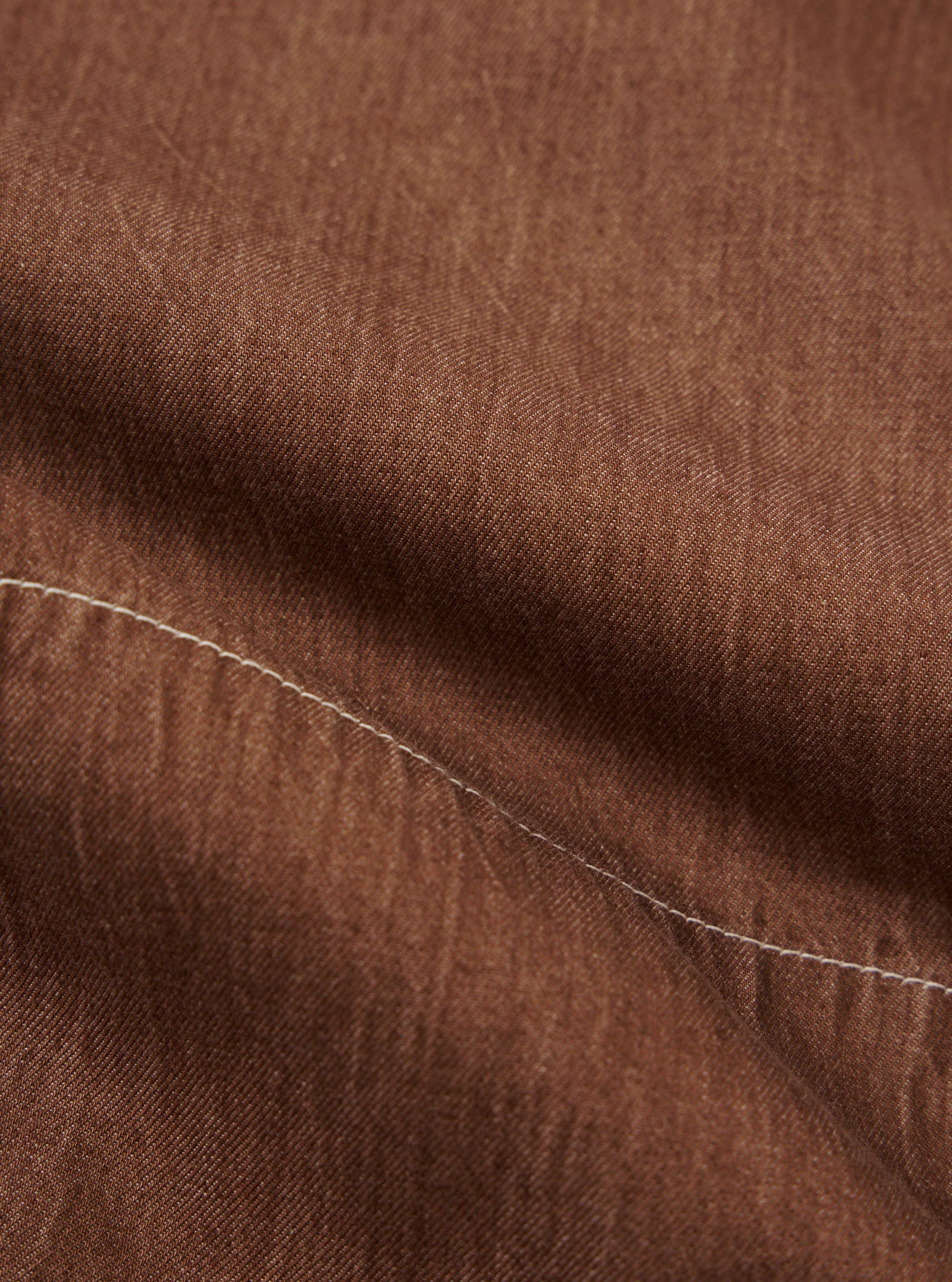 A detailed, close-up fabric swatch of the brown Meco denim used for the Marine Gilet. The image highlights the textured diagonal twill weave and the earthy brown color of the fabric.