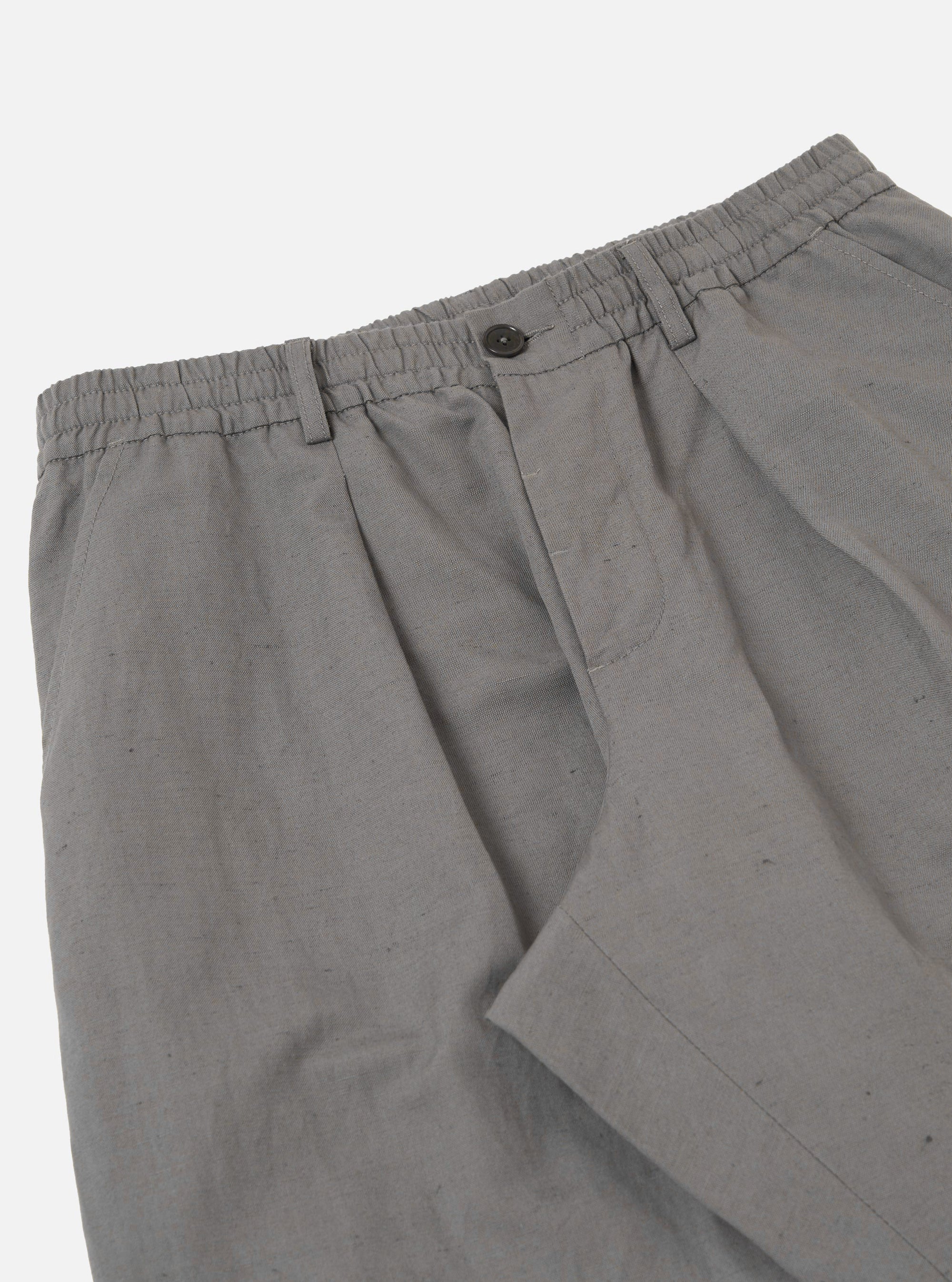 The Mid Grey Linen Slub Weave Oxford Pant is shown from the back, laid flat against a plain white background. The image highlights the two rear pockets, featuring one buttoned flap pocket and one buttoned jetted pocket, as well as the elasticated waistband and the textured slub weave of the mid-grey fabric.