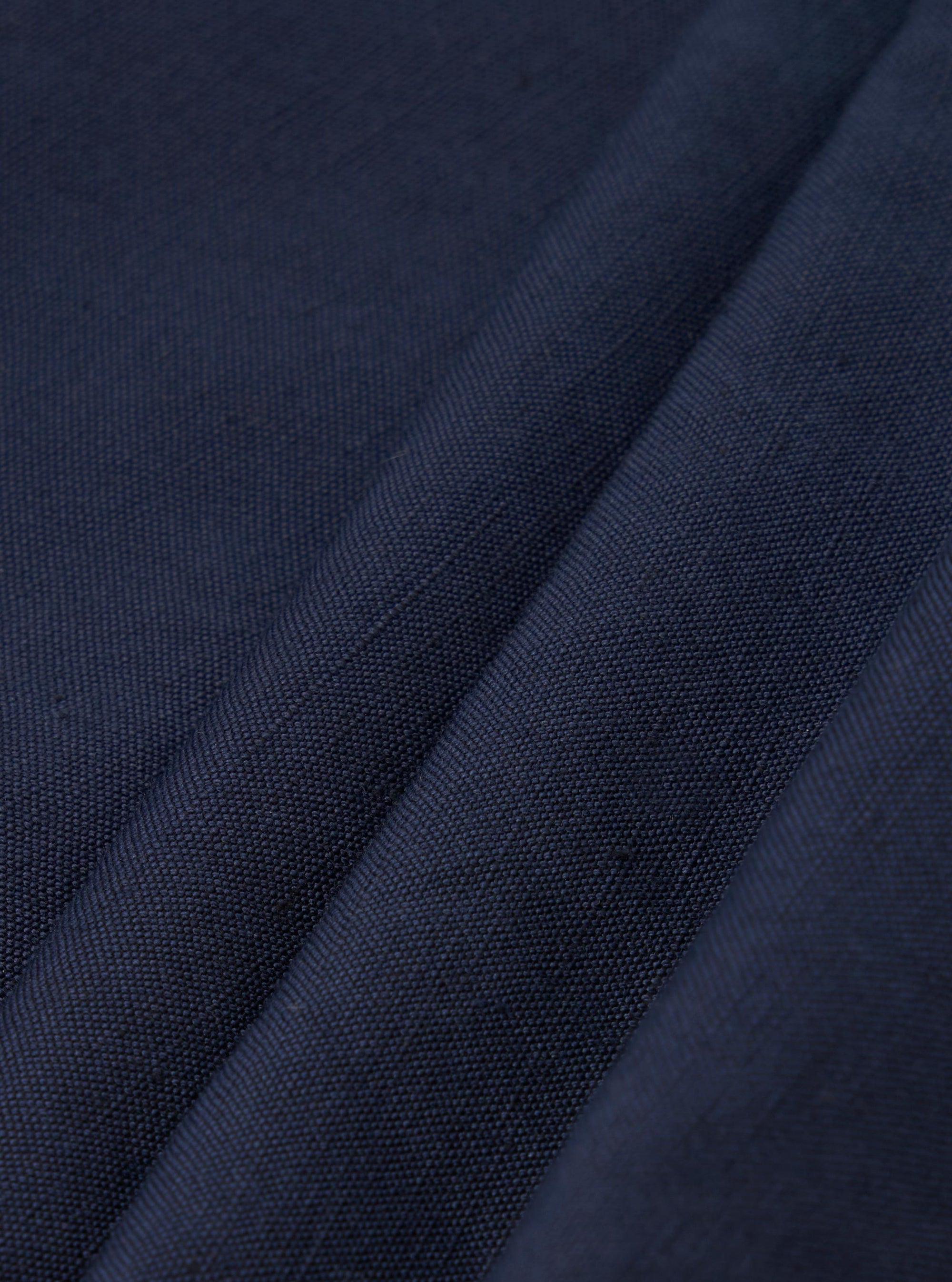A close-up fabric swatch of the Navy Linen Slub Weave Oxford Pant displays the deep navy blue material. The image highlights the textured slub weave and the blend of linen and cotton fibers.