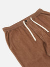 A pair of brown denim hi-water trousers is displayed flat against a plain white background. The trousers feature a slim, cropped leg and an elasticated drawstring waistband.