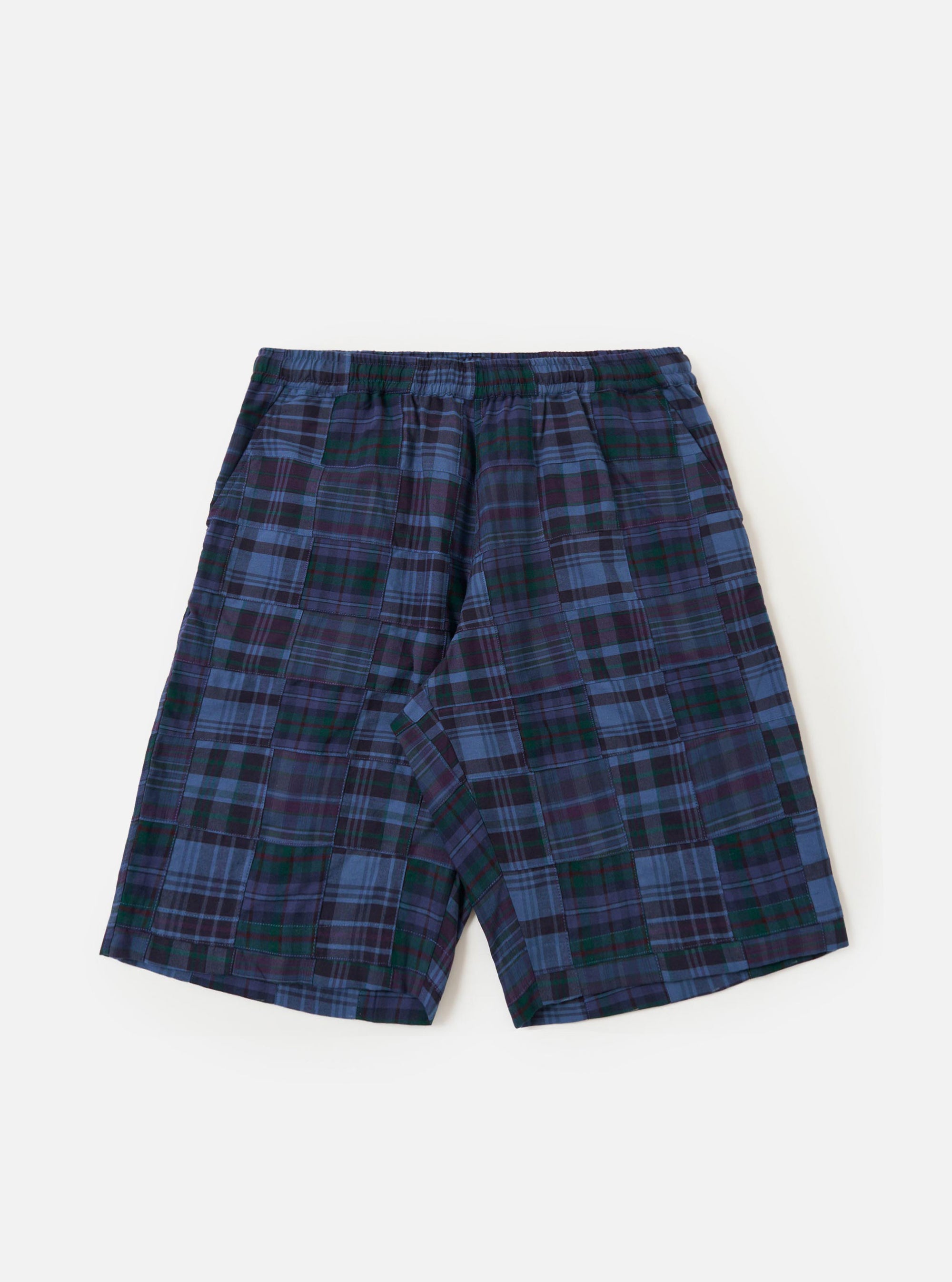 A pair of Navy Madras Patchwork Vacation Shorts is shown laid flat against a solid white background. The shorts feature a vibrant patchwork design with various shades of blue and white in a classic madras plaid pattern. Key details include an elasticated waistband with a drawstring and a relaxed, wide-leg cut.