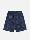 A pair of navy madras patchwork vacation shorts is shown from a rear angle, laid flat against a plain white background. The image highlights the patchwork construction of various blue and navy plaid patterns, the elasticated waistband with a drawstring, and a single rear patch pocket on the right side.
