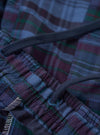 A pair of navy madras patchwork vacation shorts is displayed flat against a plain white background. The shorts feature a patchwork design of various blue and navy plaid fabrics, an elasticated waistband, and a rear patch pocket.