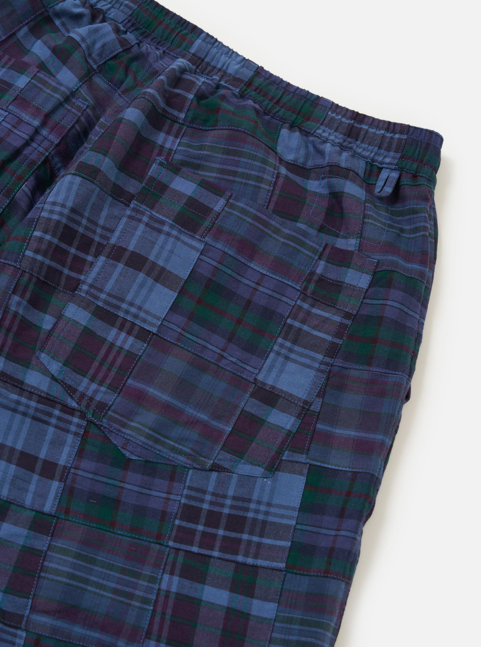 A pair of Navy Madras Patchwork Vacation Shorts is shown from a rear angle, laid flat against a solid white background. The shorts feature a mix of plaid patterns in shades of blue and navy, with two welted back pockets that include a button closure.