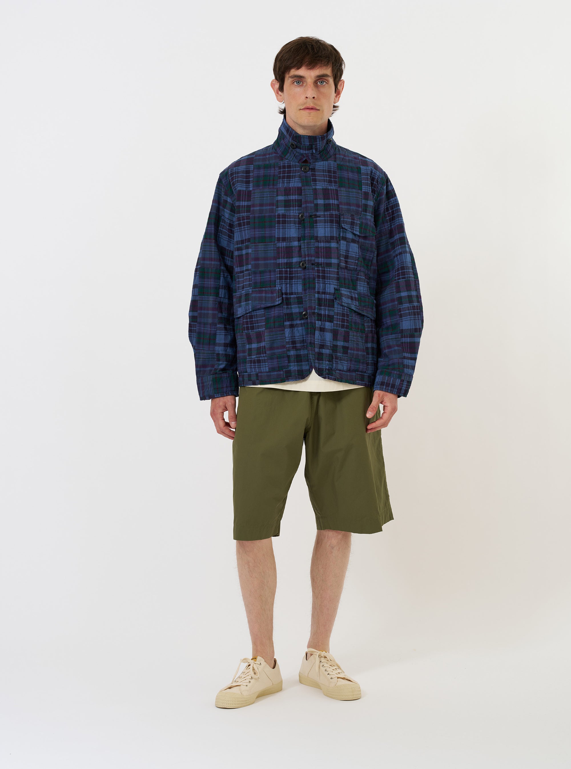 The Navy Madras Patchwork Duty Jacket is displayed flat against a plain white background. The jacket features a boxy, cropped fit and is constructed from a textured patchwork of various navy and blue plaid patterns. Prominent details include a classic pointed collar, a full button-down front, two large lower patch pockets, and a single chest pocket.