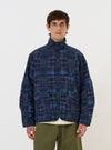 A model is wearing the Navy Madras Patchwork Duty Jacket against a plain white background. The jacket features a vibrant blue and navy madras patchwork pattern, a classic collar, and a full button-down front. The image captures the garment from the waist up, highlighting the detailed patchwork construction and utility-style design.