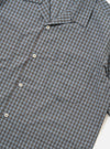 A pale blue check plaid summer overshirt is shown from the back, displayed flat against a plain white background. The image highlights the short sleeves, a straight hem with small side splits, and a horizontal yoke across the shoulders.