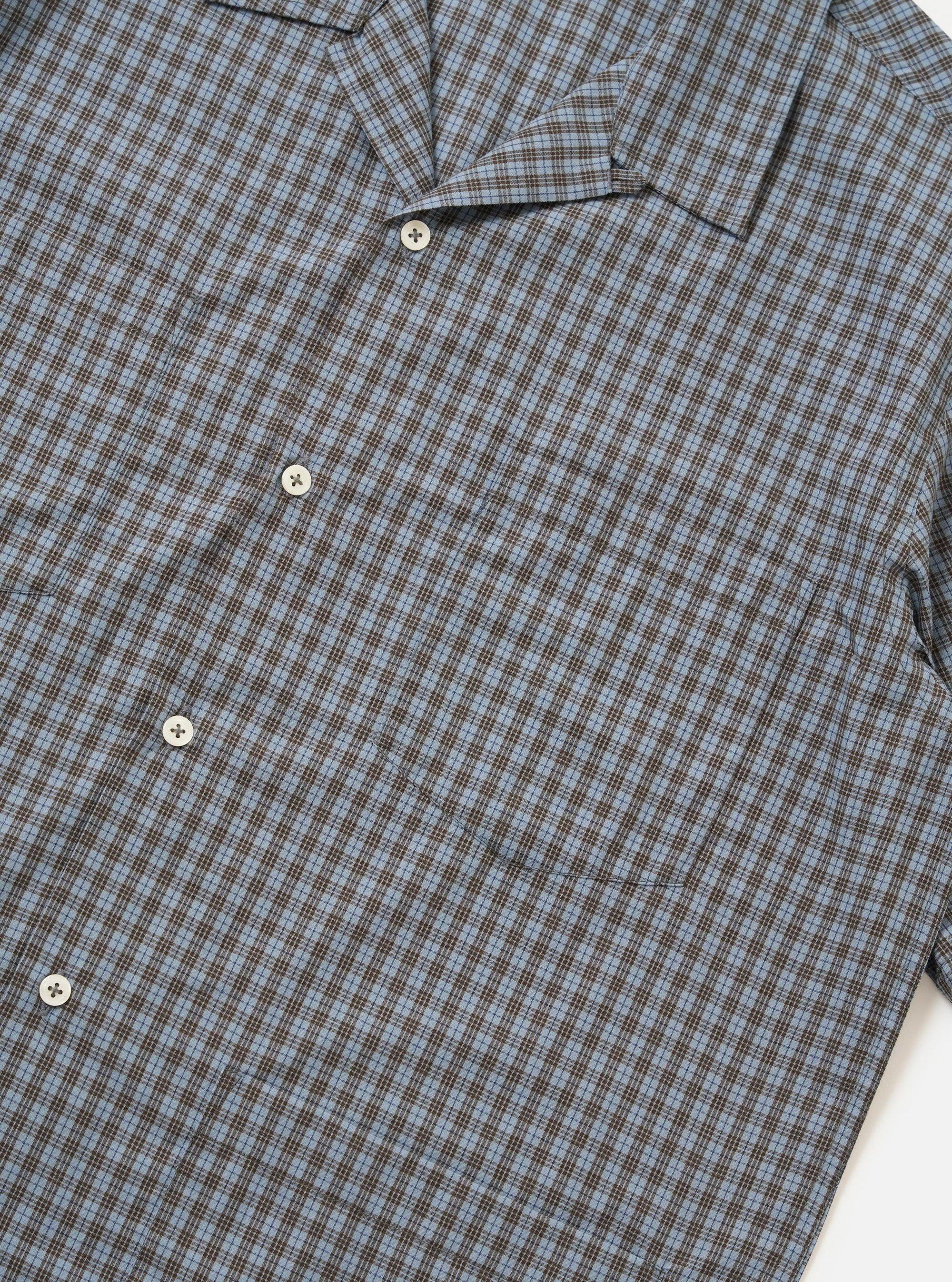 A pale blue check plaid summer overshirt is shown from the back, displayed flat against a plain white background. The image highlights the short sleeves, a straight hem with small side splits, and a horizontal yoke across the shoulders.