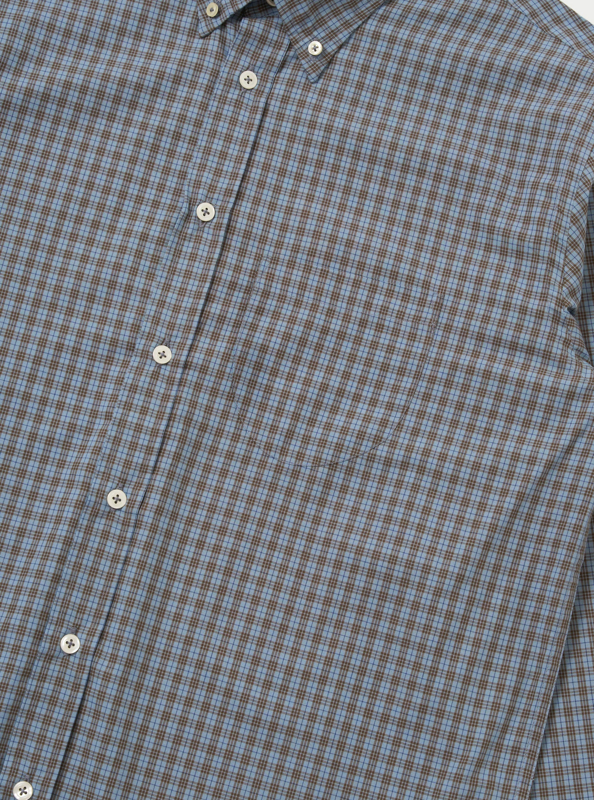 A detail shot of the Pale Blue Check Plaid Lazy Day Shirt is displayed against a plain white background. The image focuses on the chest pocket and button-down front, highlighting the pale blue and white check pattern of the fabric.
