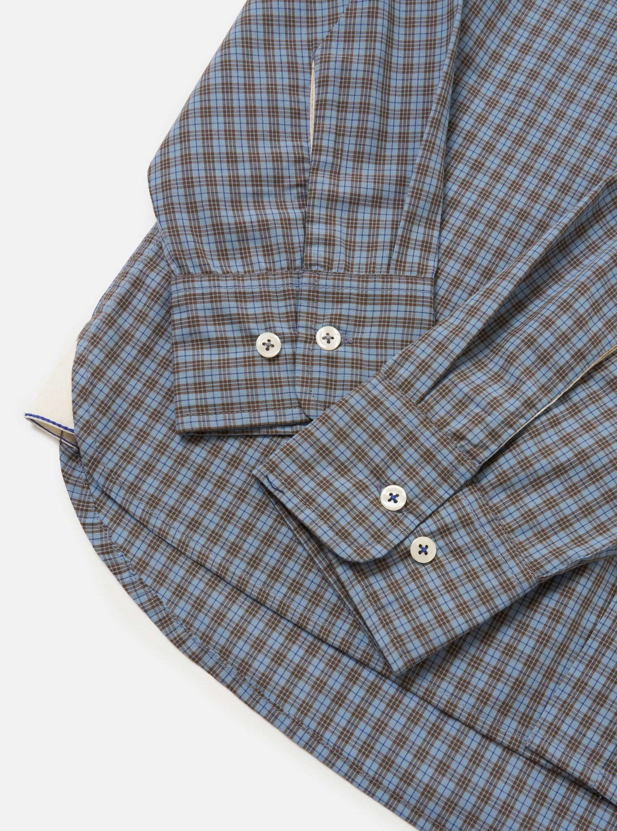 The Pale Blue Check Plaid Lazy Day Shirt is shown from the back, laid flat against a solid white background. The image highlights the back yoke and a central box pleat designed for a relaxed fit. The lightweight fabric features a small-scale blue and white check pattern.