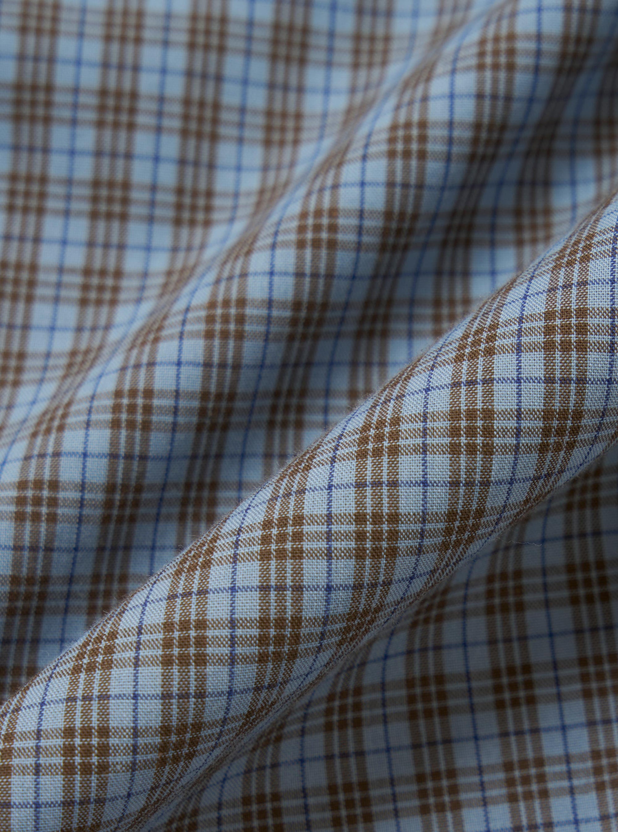A square fabric swatch shows a detailed close-up of the Pale Blue Check Plaid Lazy Day Shirt. The pattern consists of a multi-colored plaid in shades of pale blue, navy, white, and tan. The fabric texture is visible, and the image is set against a neutral, out-of-focus background.