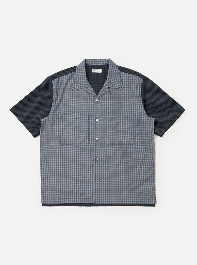 The Mixed Check Plaid Camper Shirt is shown laid flat against a white background. The shirt features a camp collar, a button-down front, and a single chest pocket on the left side. The fabric has a patchwork-style plaid pattern in various shades of blue, navy, and white.