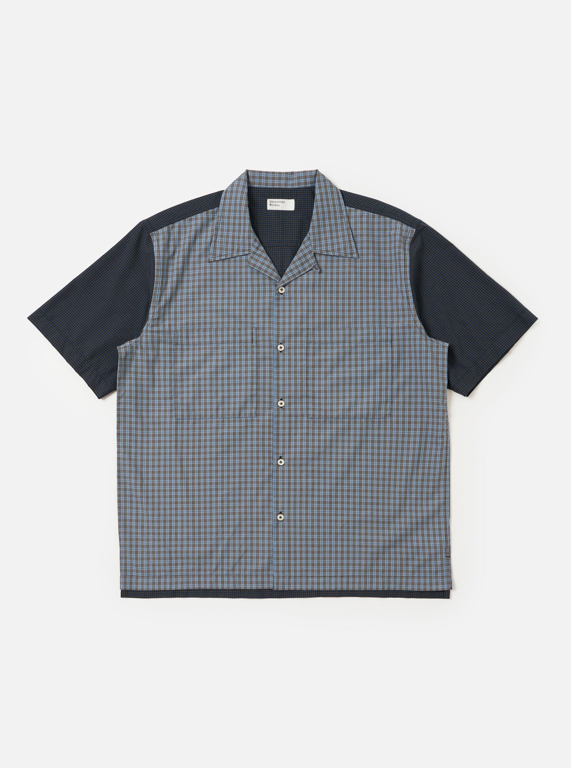 The Mixed Check Plaid Camper Shirt is shown laid flat against a white background. The shirt features a camp collar, a button-down front, and a single chest pocket on the left side. The fabric has a patchwork-style plaid pattern in various shades of blue, navy, and white.