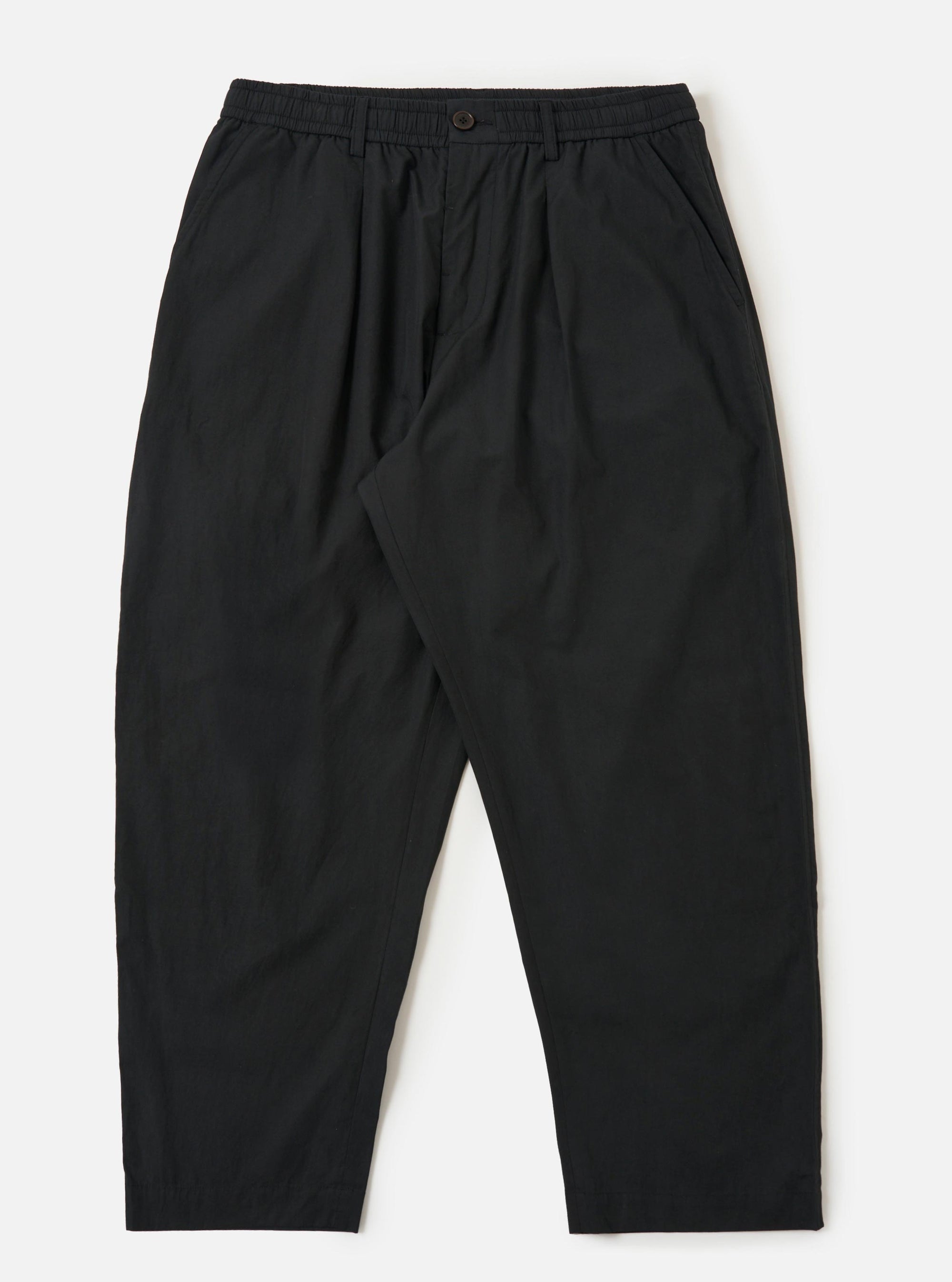 A pair of Black Broadcloth Oxford Pants is shown laid flat against a solid white background. The trousers feature a wide-leg silhouette with a single pleat on each leg and an elasticated waistband with a visible tonal drawstring. Key details include side slip pockets and a buttoned waistband.