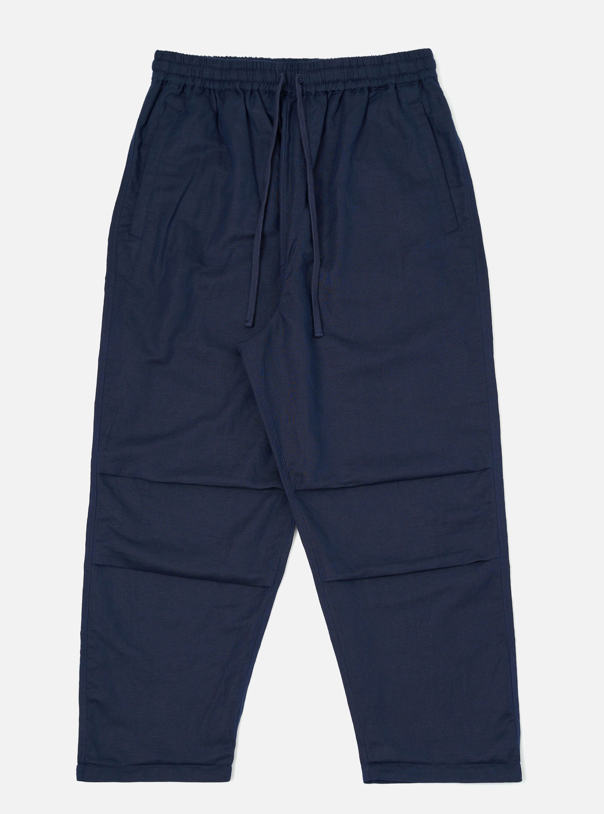 A pair of Navy Linen Cotton Shirting Parachute Pants is shown laid flat against a solid white background. The trousers feature a loose, relaxed fit with an elasticated waistband and a visible drawstring. Key details include angled front hand pockets and pronounced darting at the knees to create a structured, curved leg silhouette.